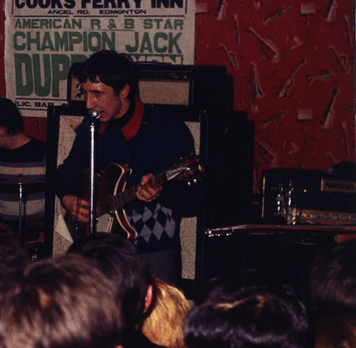 Ca. 1965, with Fender Pro head on top of single Marshall 4×12 on stand (with torn speaker grille cloth). Guitar is Rickenbacker 360/12 Export 12-string, with 1997 or 1998 6-string at right on table. (Marshall amp in back is likely another group’s.) 